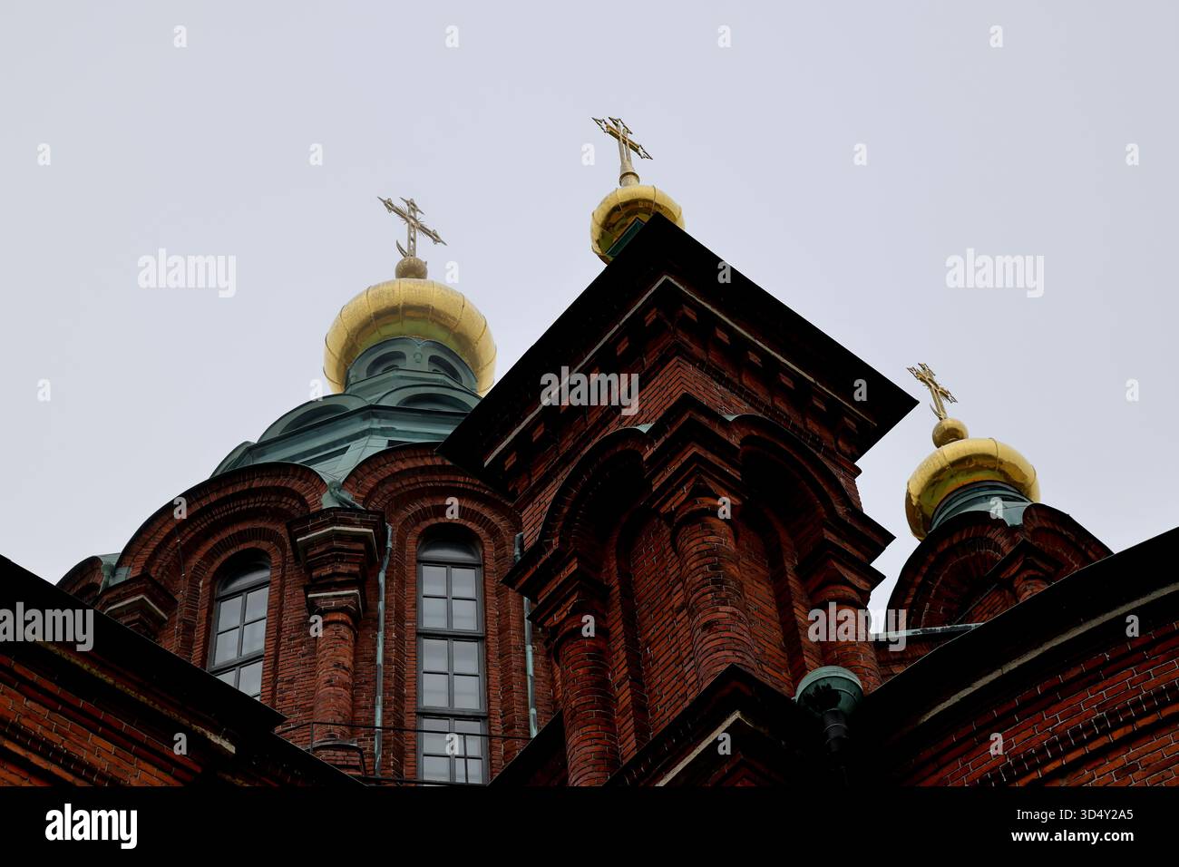 Les dômes supérieurs et les flèches de la cathédrale d'Uspenski avec des croix dorées et des pilastres de briques à Helsinki, en Finlande, photographiés vers le haut dans un ciel blanc brumeux. Banque D'Images