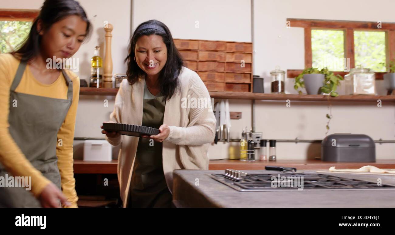 Préparation de deux femmes portant des tabliers mélangeant et tenant une poêle à tarte cannelée dans la cuisine avec table de cuisson à gaz Banque D'Images