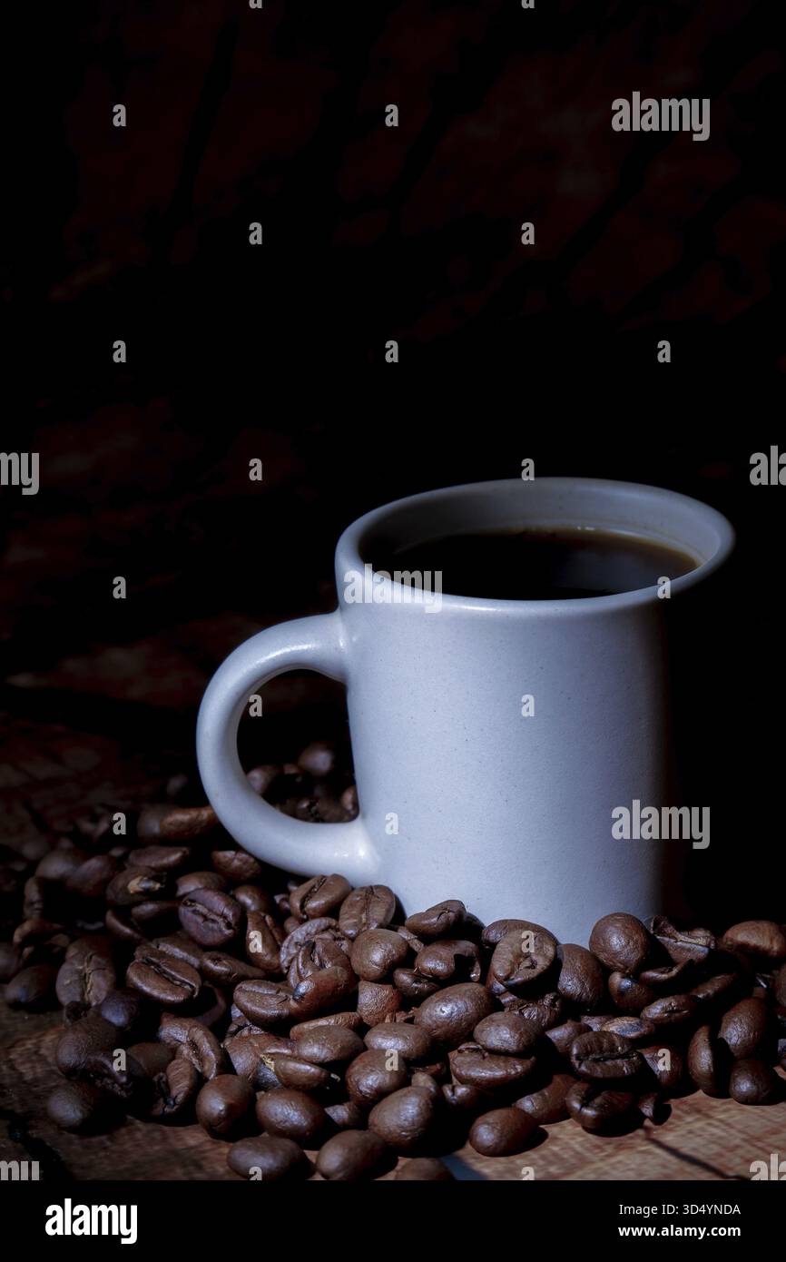 Cuire du café chaud à la vapeur dans une tasse blanche debout parmi des grains d'arabica torréfiés foncés sur une surface en bois brun Banque D'Images