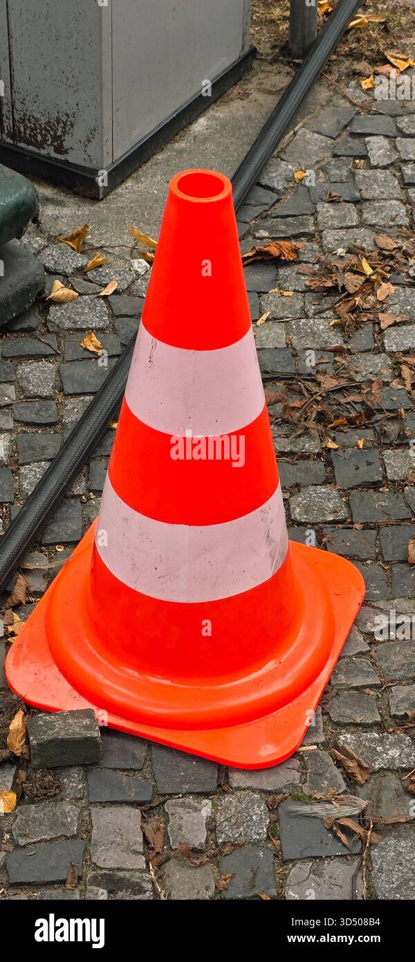 Berlin, Allemagne - 22 septembre 2025 : cône de circulation orange vif placé sur une rue pavée avec des feuilles tombées autour. - Image de stock capturée avec un smartphone