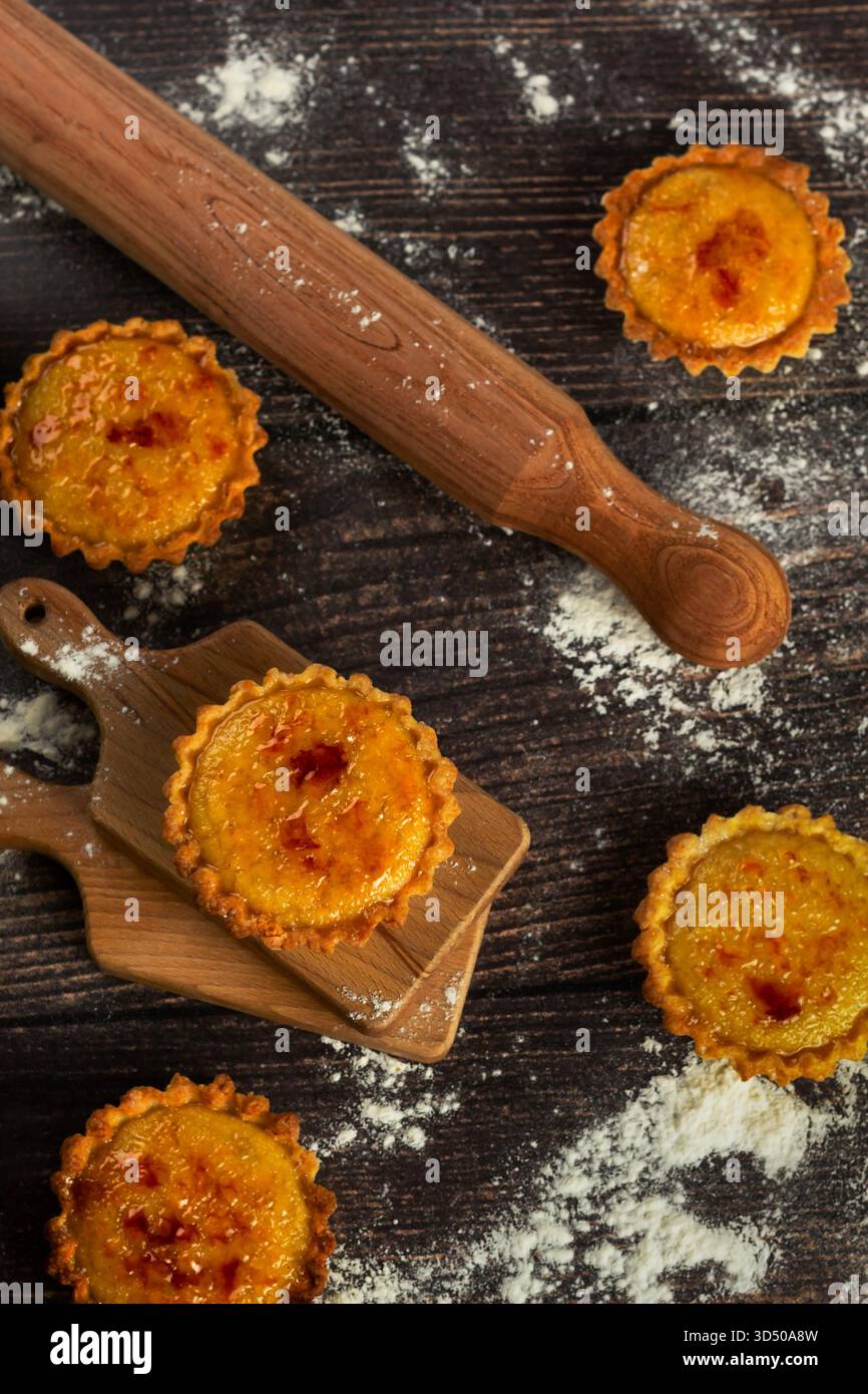 Tartes fraîches du four reposent sur une planche de bois. Un rouleau à pâtisserie et de la farine dépoussièrent la table de cuisine sombre, capturant un moment de joie de cuisson. La couleur chaude Banque D'Images