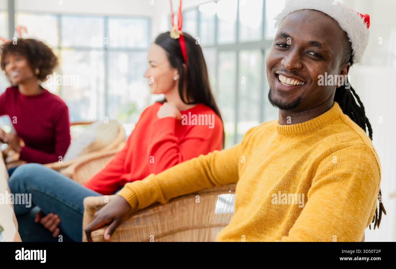 Amis divers se prélassant sur des chaises en osier dans le salon portant un chapeau de Père Noël près des fenêtres, espace de copie Banque D'Images