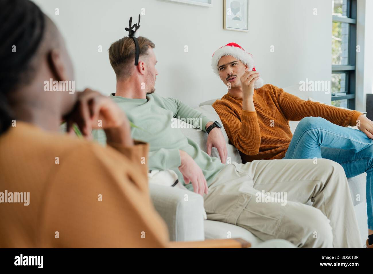 Divers amis masculins discutant à la maison sur le canapé portant des chapeaux de fête près de l'art encadré, espace de copie Banque D'Images