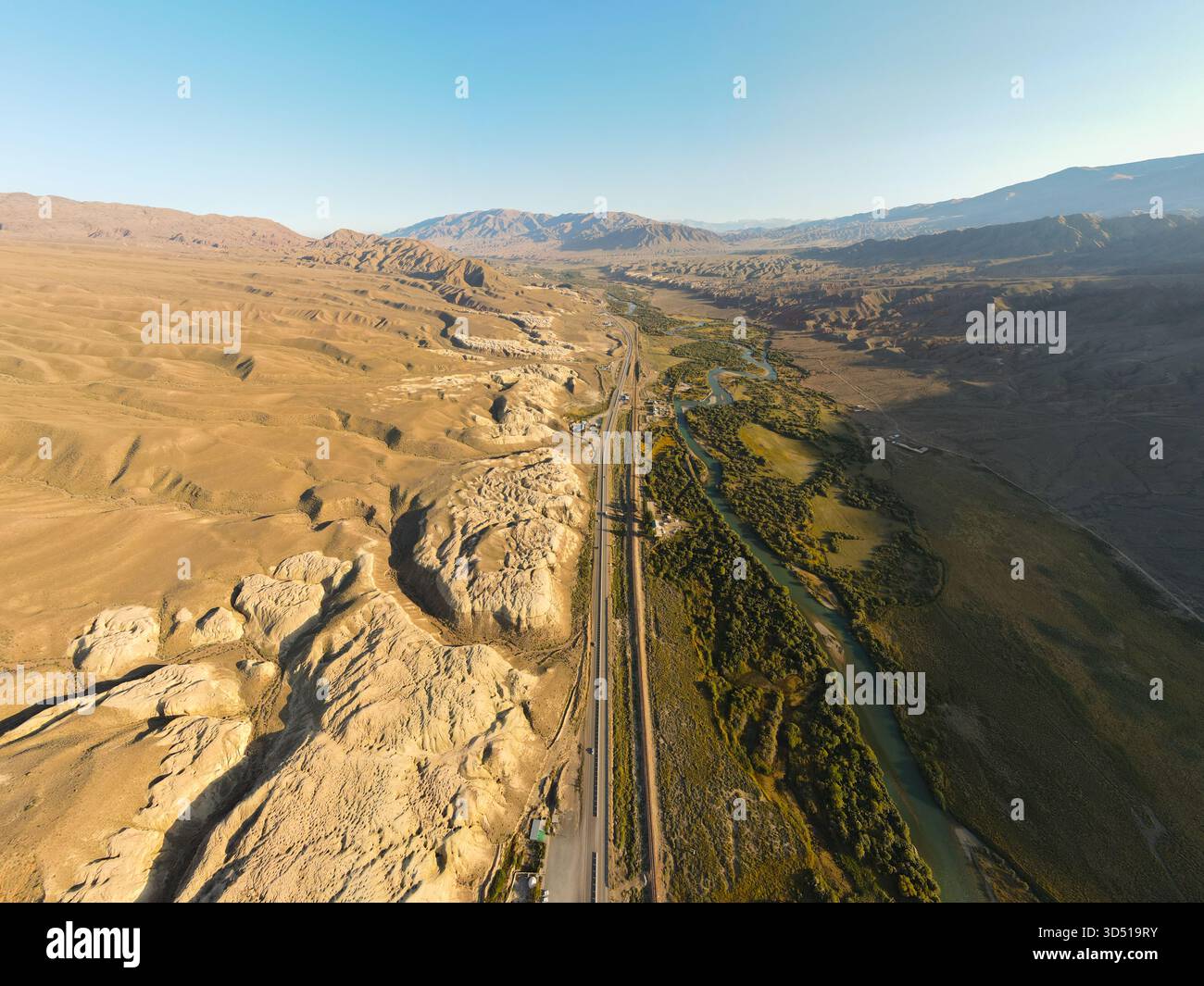 Une vue aérienne à haute altitude d'une autoroute droite et d'une rivière sinueuse coupant à travers une vallée de montagne sèche et aride avec des jaunes texturés fortement érodés Banque D'Images