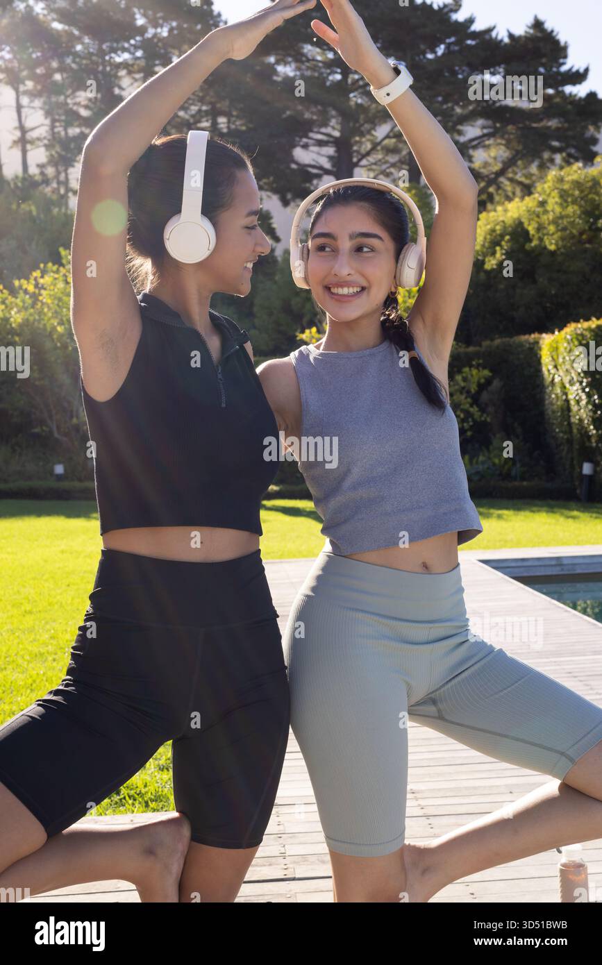 Équilibrer diverses amies féminines formant une arche de yoga sur une terrasse en bois, avec des écouteurs et une bouteille d'eau Banque D'Images