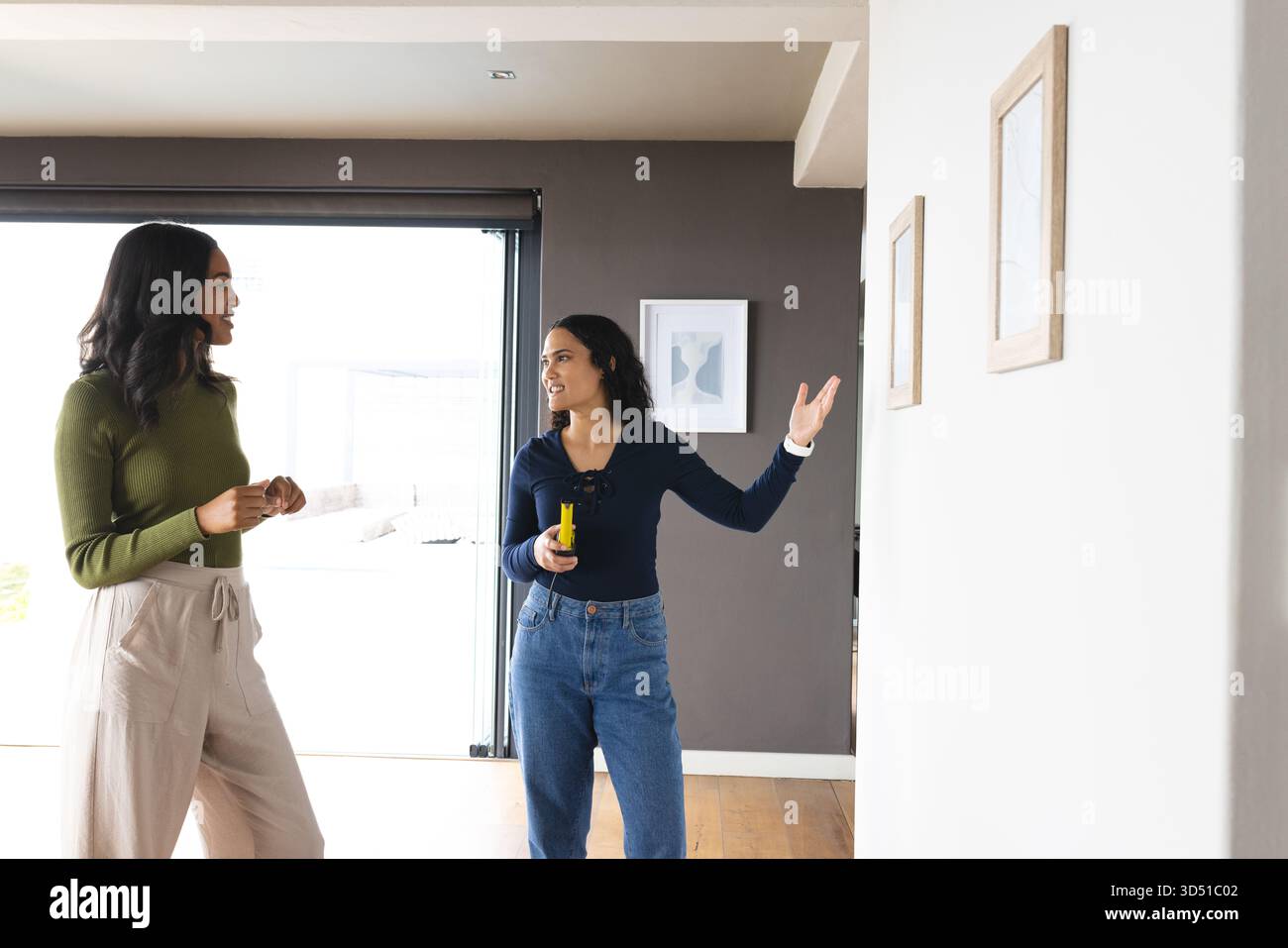 Positionnement de cadres en bois divers amis féminins debout à la porte dans la maison, avec mètre laser jaune Banque D'Images