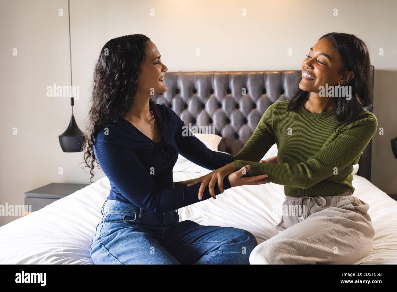 Souriant diverses amies féminines assises sur le lit avec tête de lit touffetée dans la chambre, avec des lumières suspendues Banque D'Images