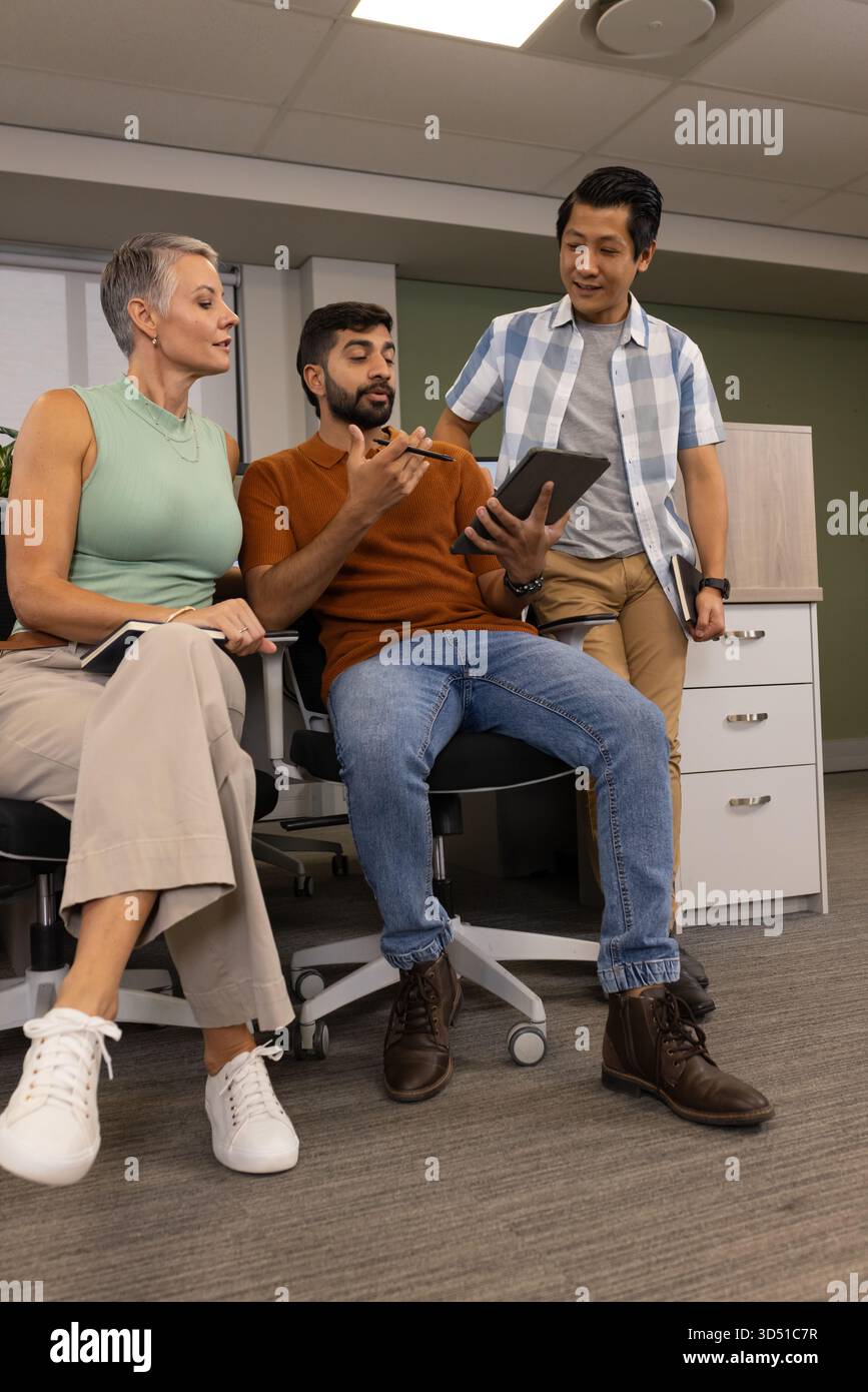 Collaboration de divers collègues discutant de projets au siège social, à l'aide d'une tablette et d'un ordinateur portable Banque D'Images