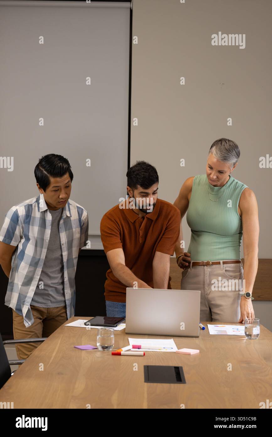 Examen de divers collègues examinant des cartes et un ordinateur portable à la table de la salle de réunion, avec tablette Banque D'Images