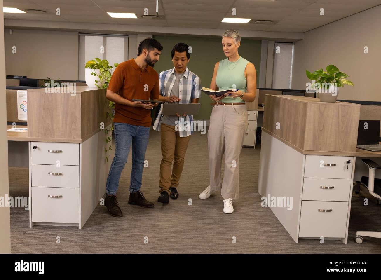 Collaboration de plusieurs collègues examinant le rapport dans l'allée de l'armoire, avec tablette, ordinateur portable et ordinateur portable Banque D'Images