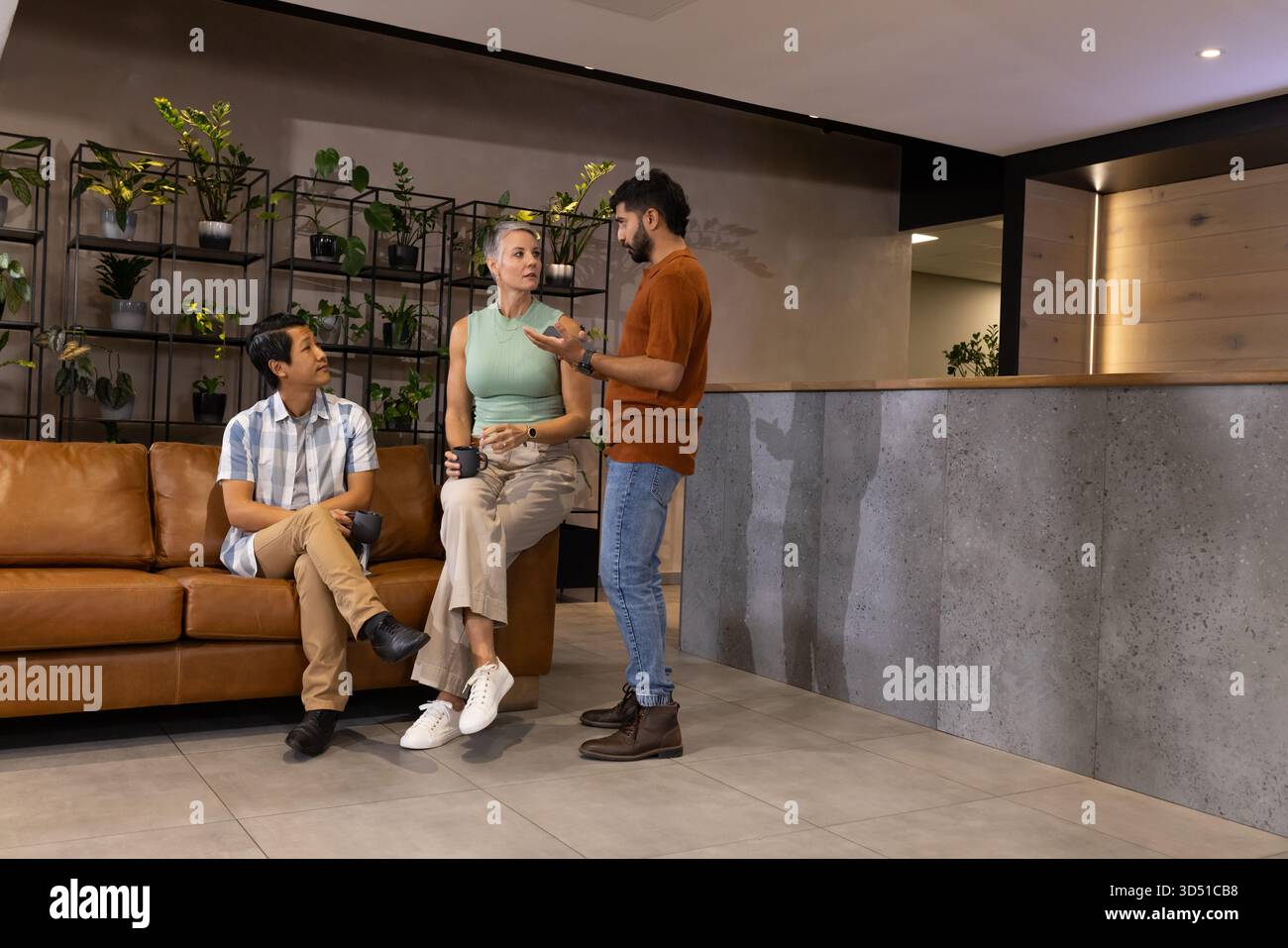 Parler divers collègues assis et debout dans le salon de bureau, avec tasse à café et smartphone Banque D'Images