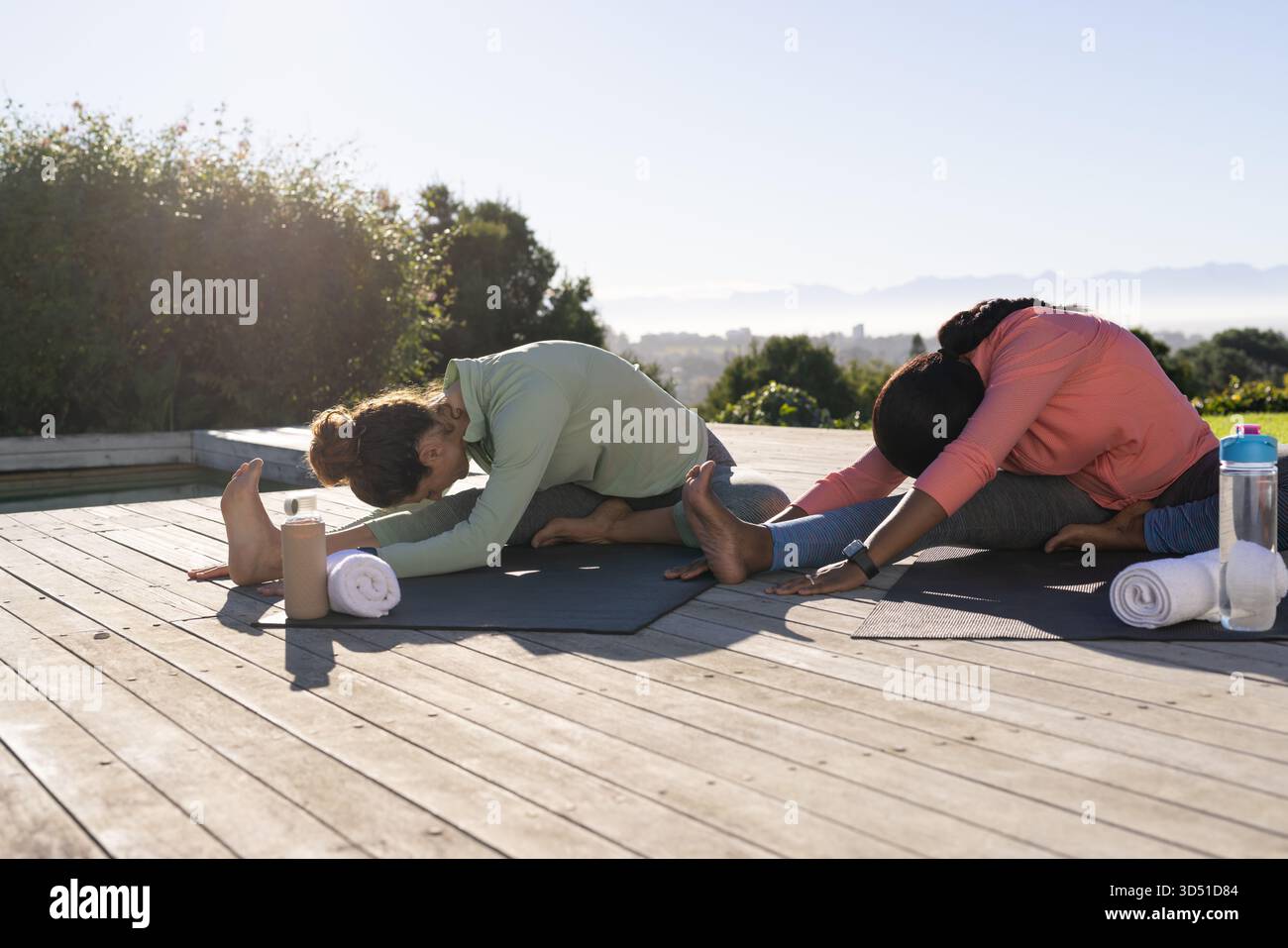 Étirer diverses amies atteignant les jambes sur le pont, avec des tapis de yoga, des serviettes et des bouteilles d'eau Banque D'Images