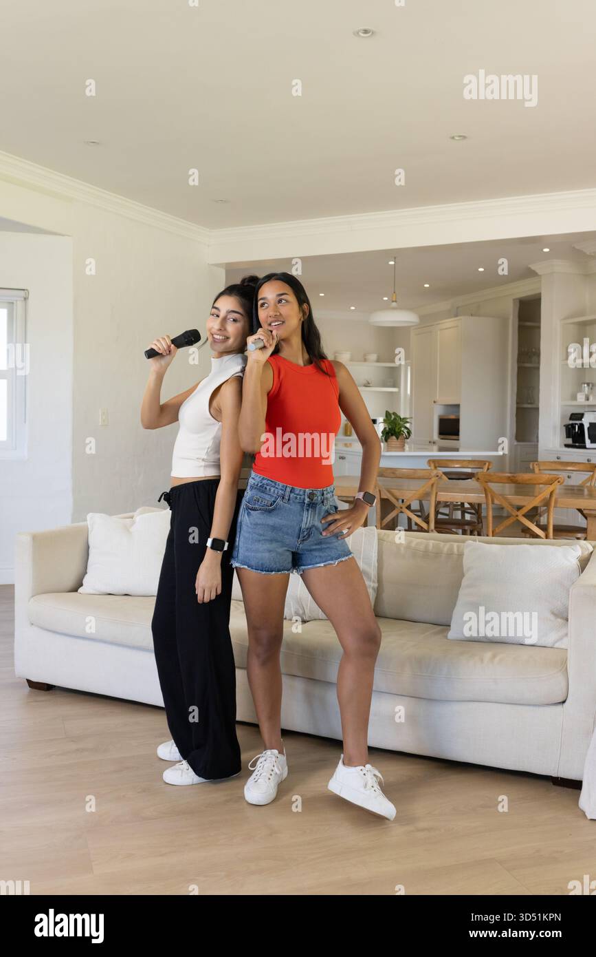 Chant karaoké diverses amies féminines à l'aide de microphones sans fil dans le salon lumineux, avec canapé Banque D'Images
