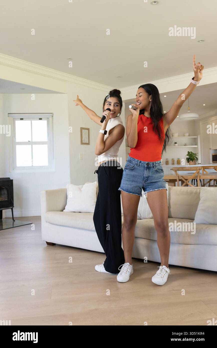 Chanter diverses amies féminines dansant avec des microphones sans fil dans le salon lumineux Banque D'Images