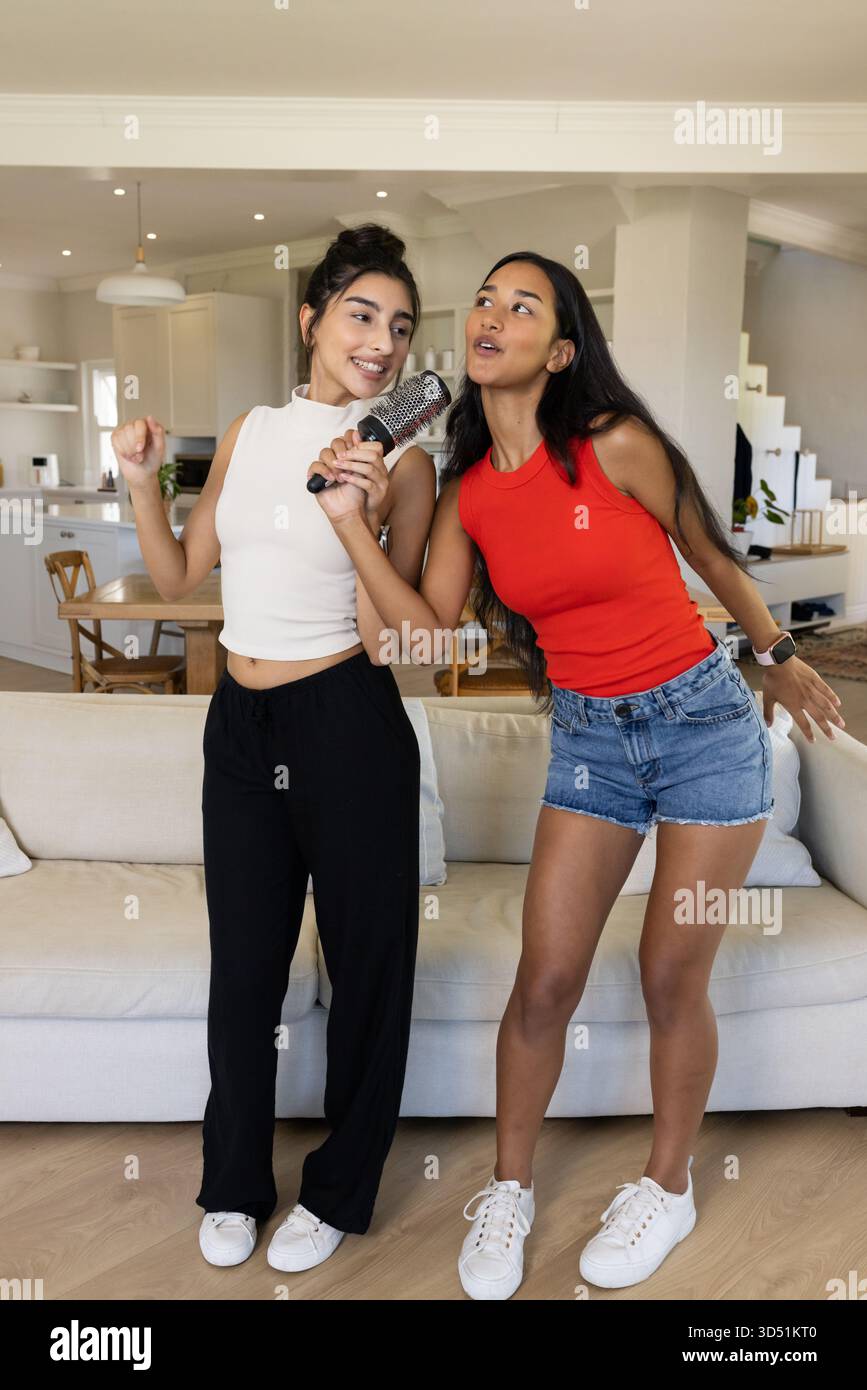 Tenant la brosse à cheveux, diverses amies chantant dans le salon et la cuisine, avec des lumières suspendues Banque D'Images