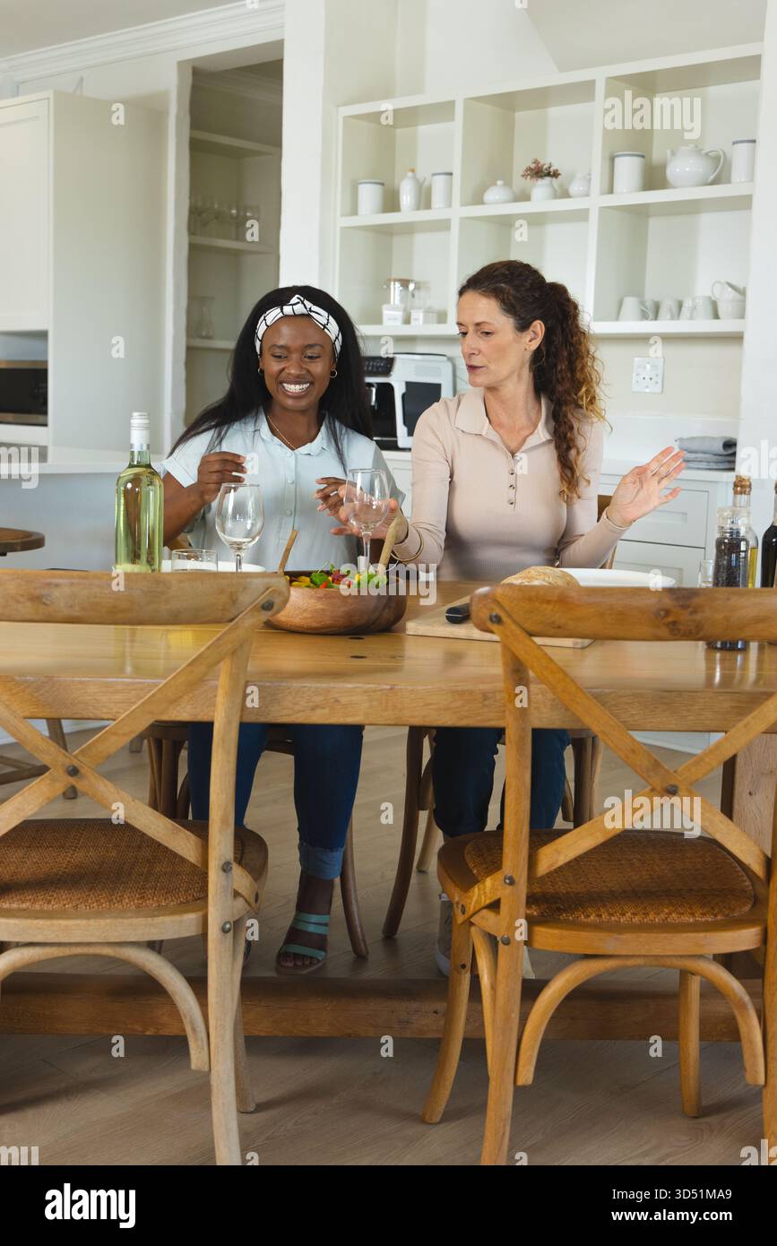 Clinking verres à vin diverses amies féminines riant à la table à manger de la ferme, avec saladier Banque D'Images