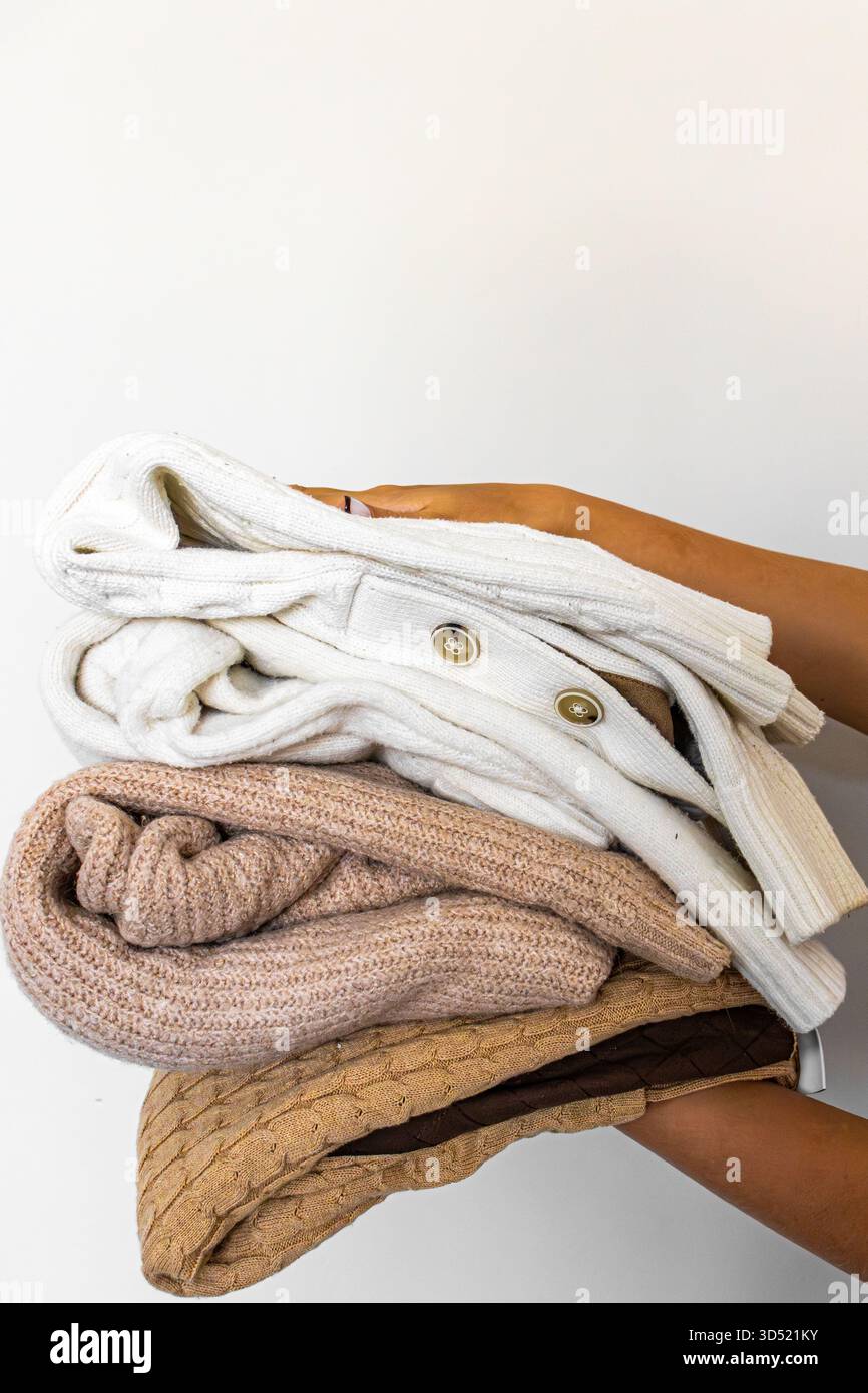 Un ensemble de pulls tricotés chauds dans des tons clairs et beiges, soigneusement pliés et tenus dans vos mains. Banque D'Images
