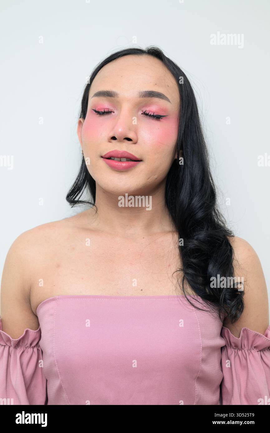 Portrait studio d'un jeune transgenre thaïlandais avec maquillage et cheveux longs. Concept d'expression de genre, fierté LGBTQ et inclusivité montrant un Banque D'Images