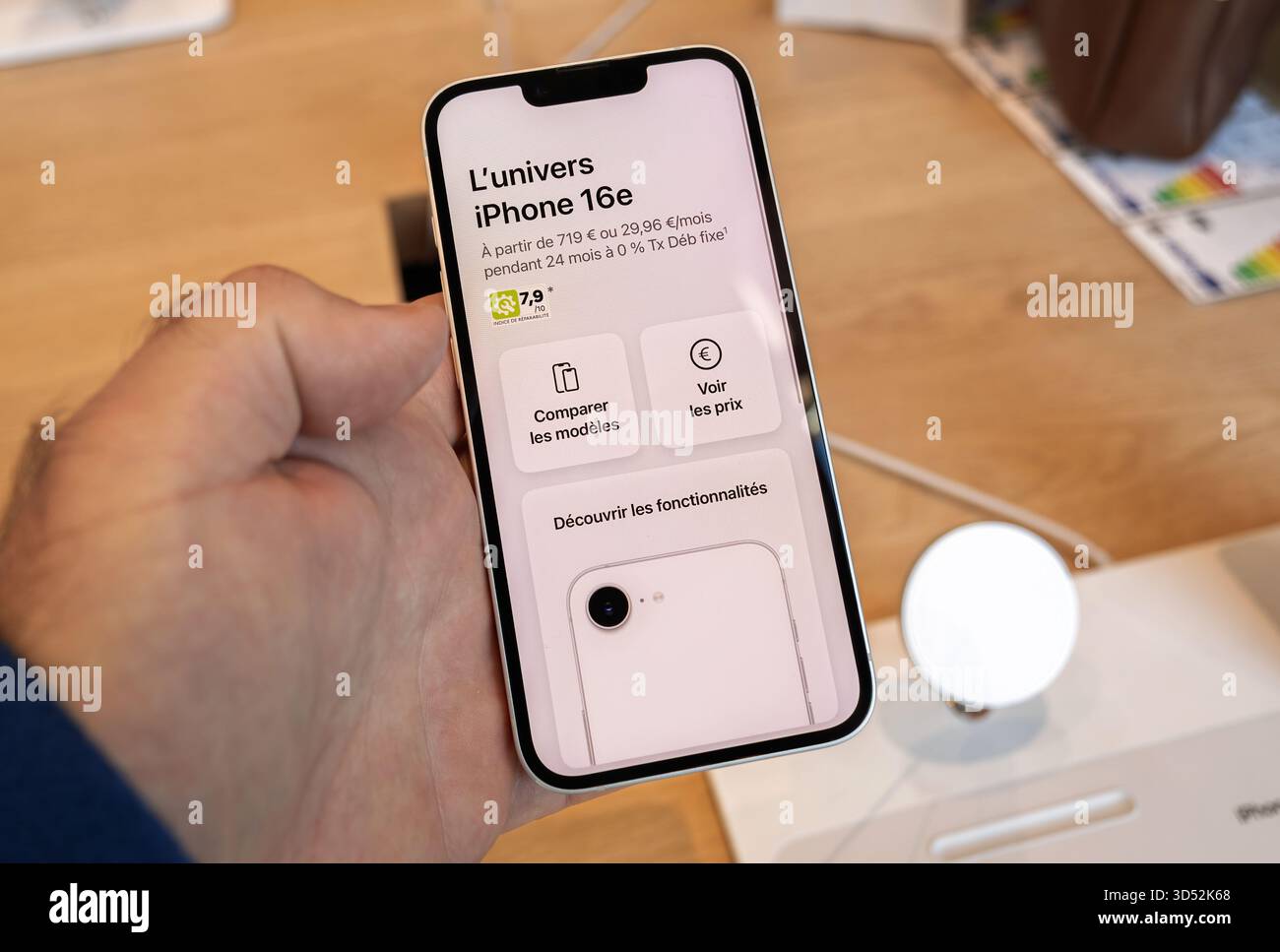 Paris, France - Sep 19, 2025 : gros plan de Hand Holding Apple iPhone 16e montrant l'écran avec le prix, les spécifications et les options de comparaison en français à o Banque D'Images
