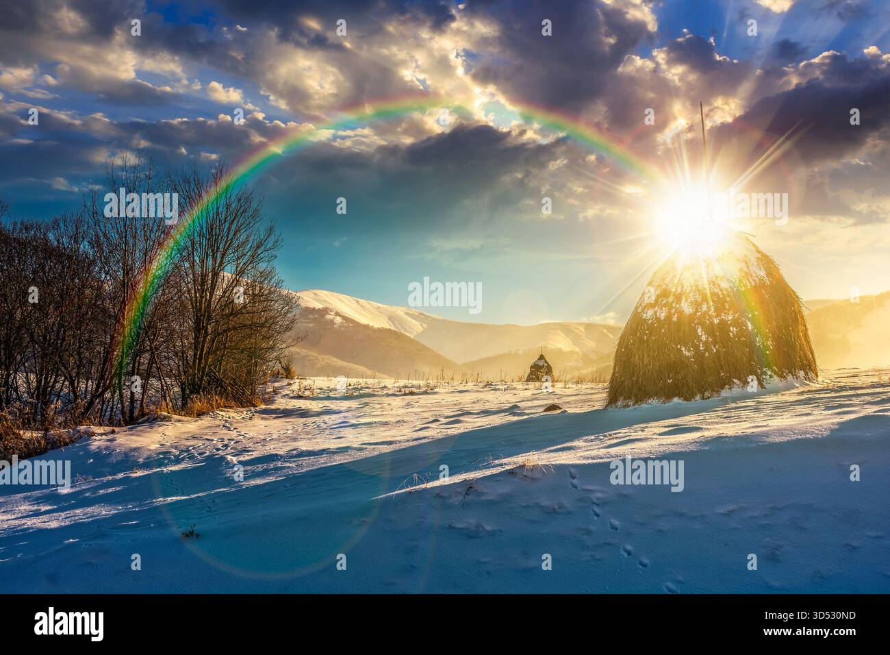 paysage rural avec meule de foin en hiver au coucher du soleil. paysage de campagne avec colline couverte de neige dans les montagnes dans la lumière du soir. vue en bas angle avec neige Banque D'Images