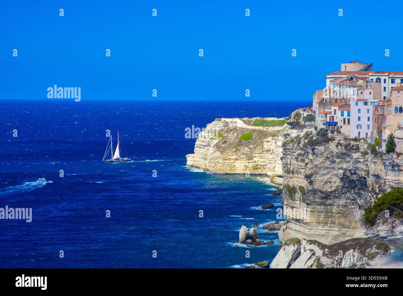 Vue sur la ville médiévale de Bonifacio avec sa côte de calcaire blanc et sa mer turquoise d'un bleu profond et rude et bateau à voile sous le soleil et le ski bleu Banque D'Images