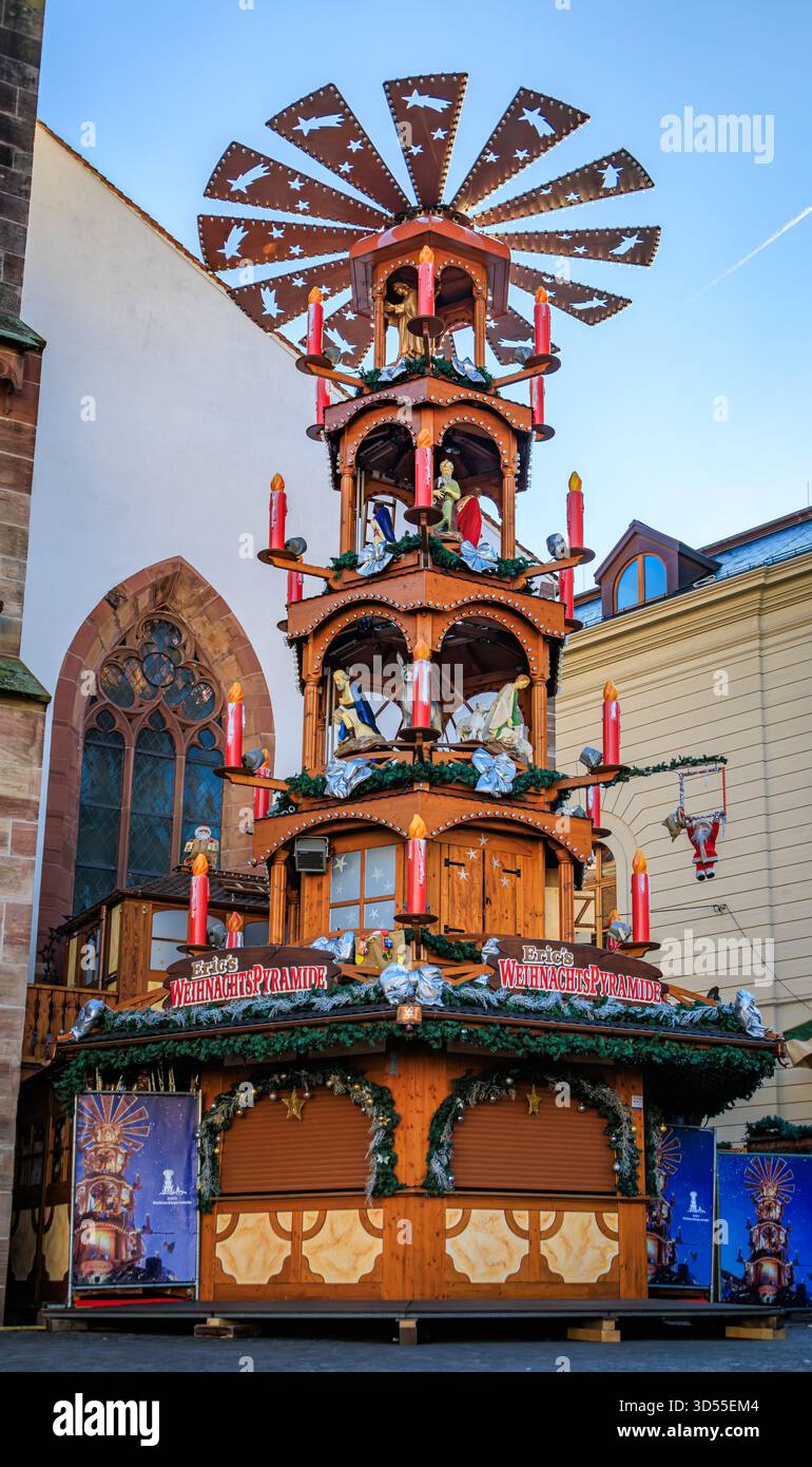 Bâle, Suisse - 16 novembre 2024 : Grande pyramide de Noël traditionnelle en bois avec des figures de la crèche et des bougies rouges au marché de Noël Banque D'Images
