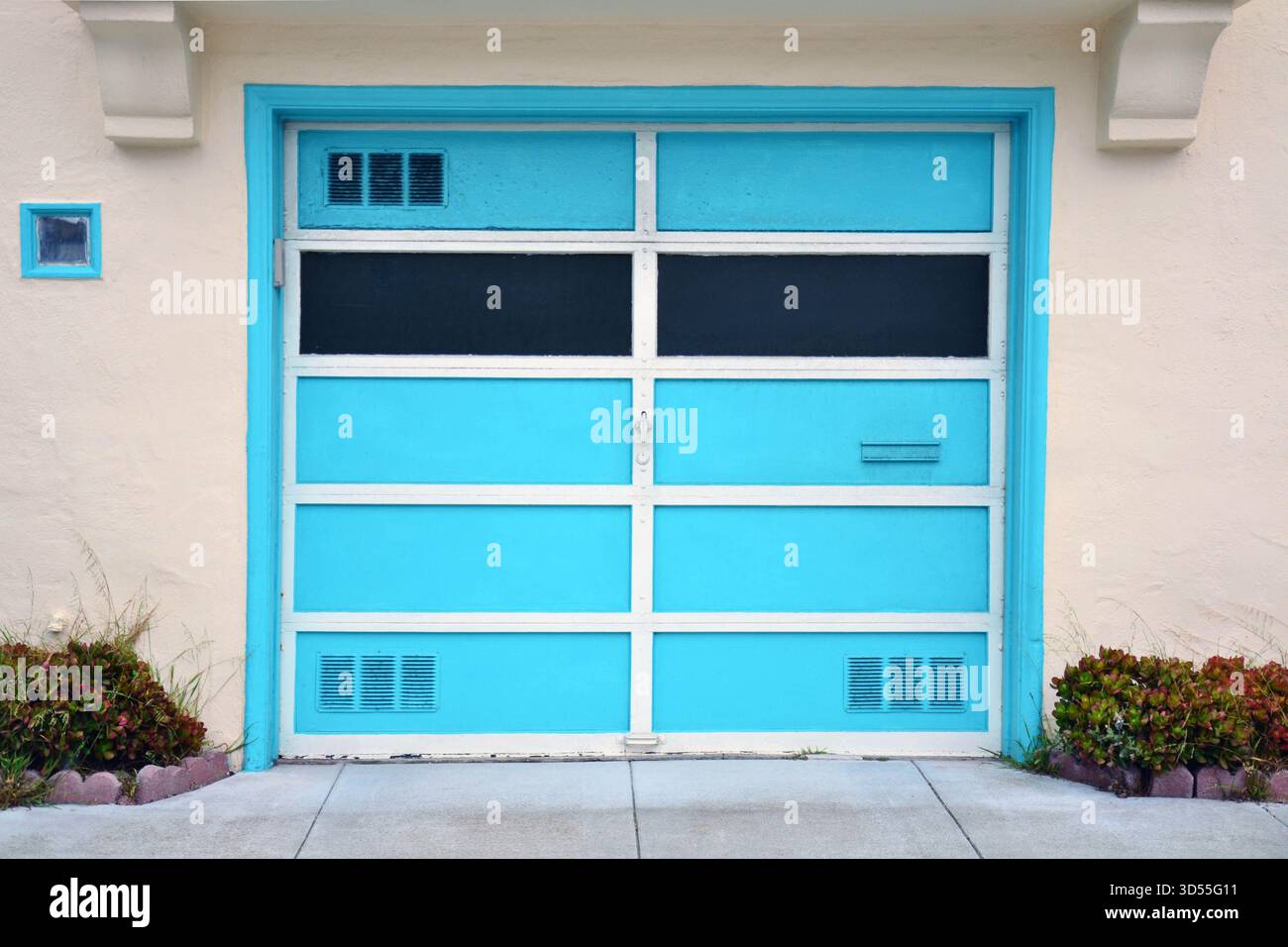 Porte de garage turquoise lumineuse avec garniture blanche sur une maison beige à San Francisco, avec des lignes épurées, un contraste de couleur audacieux et un design architectural simple Banque D'Images
