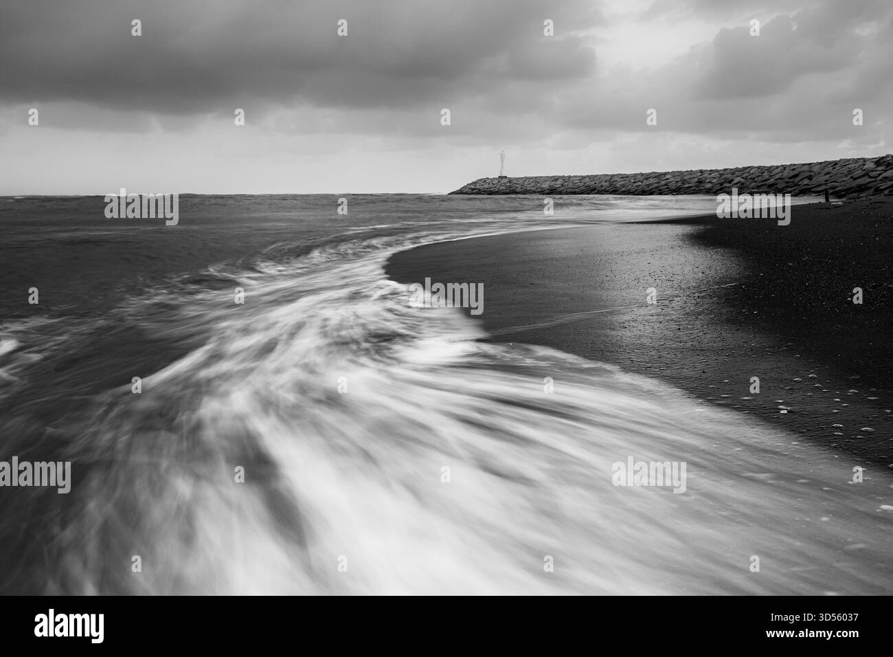 Noir et blanc longue exposition des vagues tourbillonnant sur une plage rocheuse rivage avec ciel dramatique et mouvement de l'eau texturé. Banque D'Images