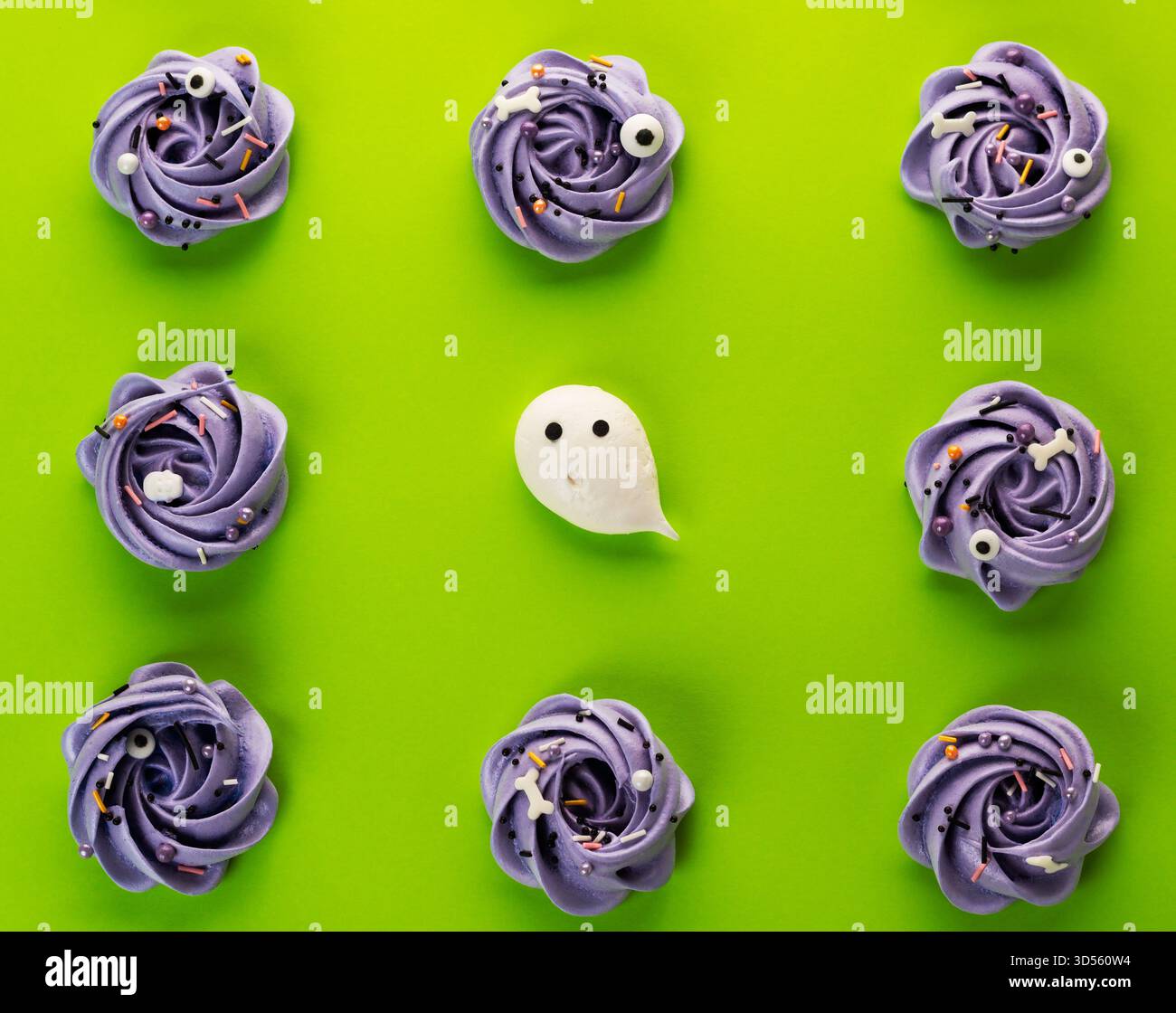 Neuf cupcakes pourpres décorés avec des décorations fantomatiques sont disposés sur un fond vert vif, parfait pour une fête d'Halloween ou une célébration. Banque D'Images