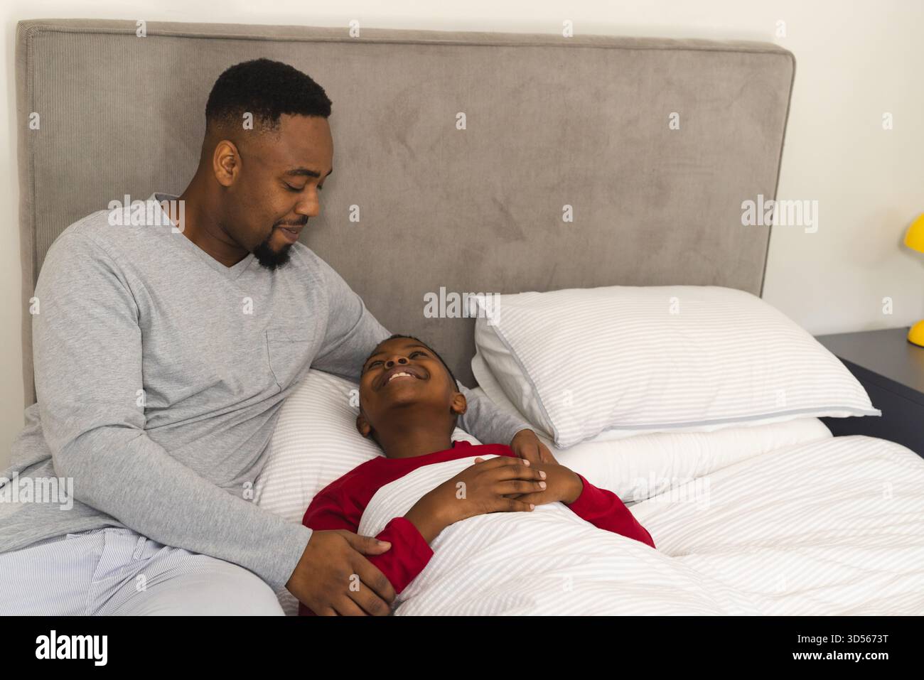 Père afro-américain réconfortant son fils au lit, partageant un moment joyeux à la maison Banque D'Images