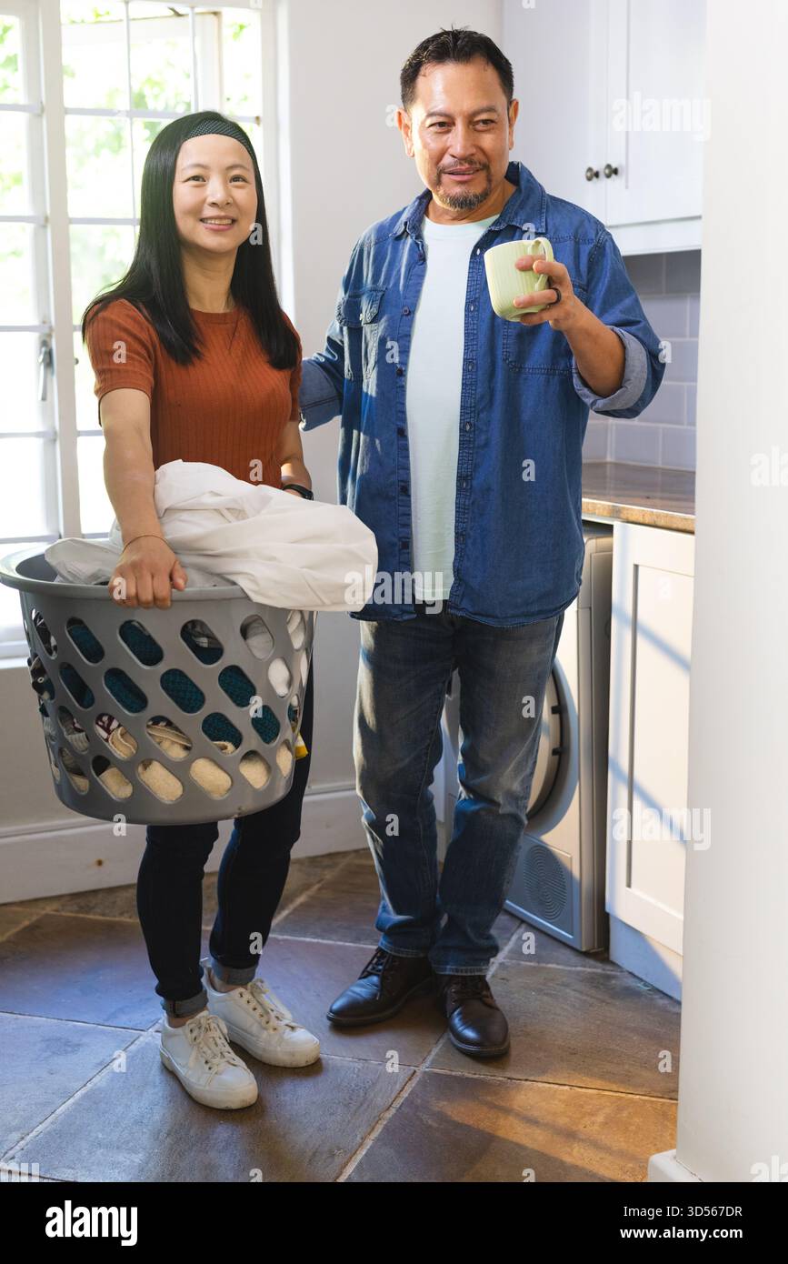 Couple mature faisant la lessive ensemble à la maison, souriant et appréciant le café Banque D'Images