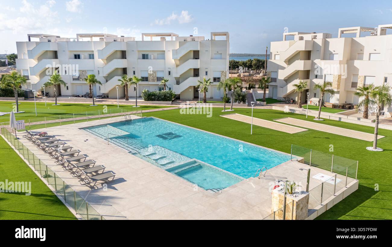 Vaste piscine avec chaises longues, aménagement paysager verdoyant et bâtiments blancs de style méditerranéen dans un complexe résidentiel. Banque D'Images