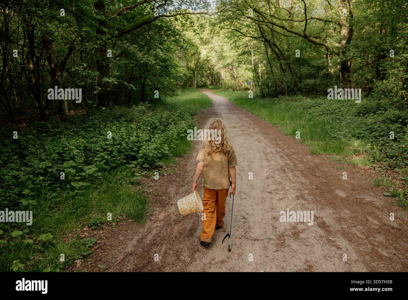 Enfant marchant seul sur un chemin forestier avec seau et bâton Banque D'Images
