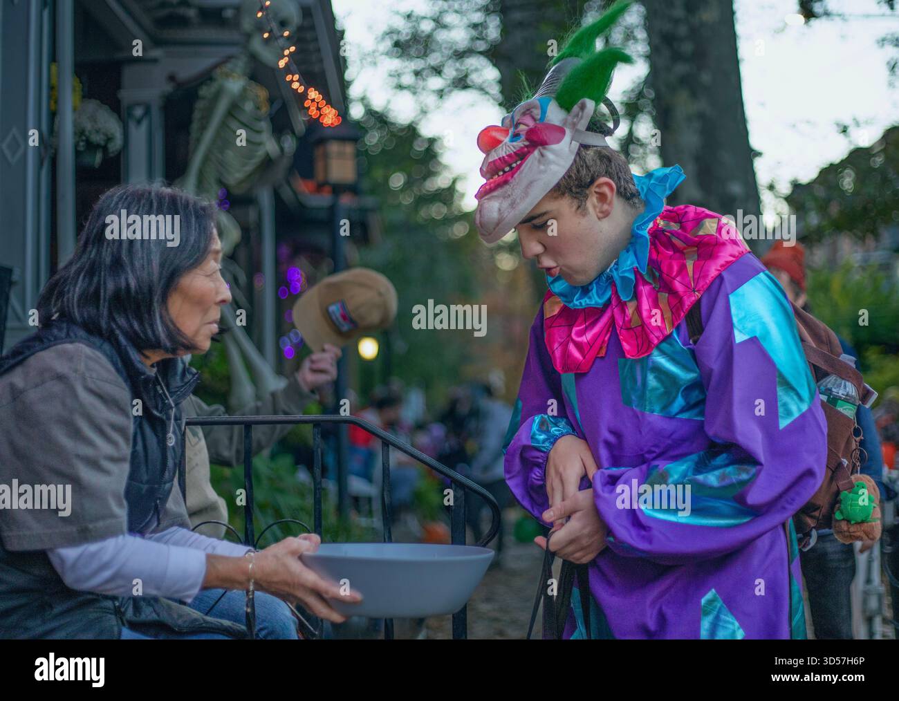 Un adolescent habillé comme un clown trick-or-traite une femme à Halloween. Banque D'Images