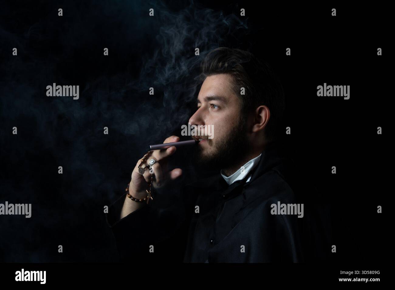 Un prêtre dans son uniforme d'église avec une cigarette dans la bouche et un chapelet dans les mains Banque D'Images