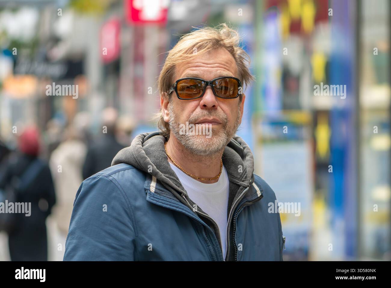 Un homme âgé de 50-55 ans portant des lunettes noires se tient dans la rue parmi les passants en mouvement Banque D'Images