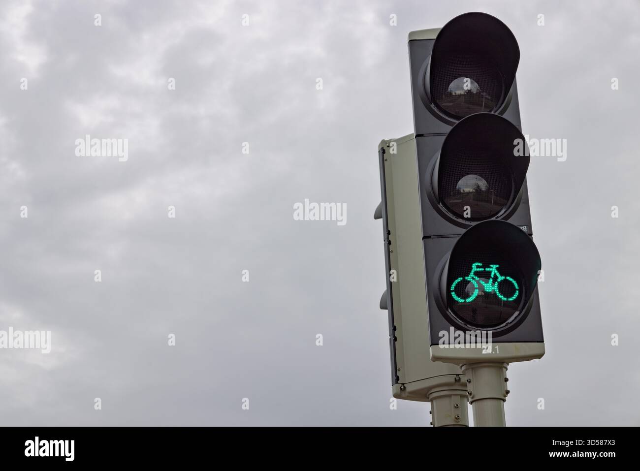 Gros plan d'un feu de circulation néerlandais moderne pour vélos, montrant un feu vert éclatant contre un ciel nuageux et discret, guidant les cyclistes. Banque D'Images