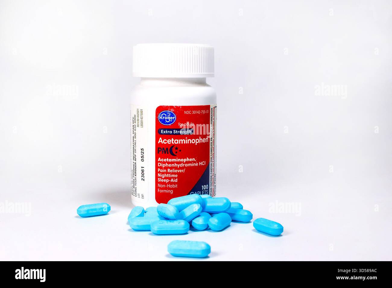 Bouteille blanche de caplets PM acétaminophène Kroger avec étiquette rouge entourée de pilules bleues éparpillées sur fond blanc Banque D'Images
