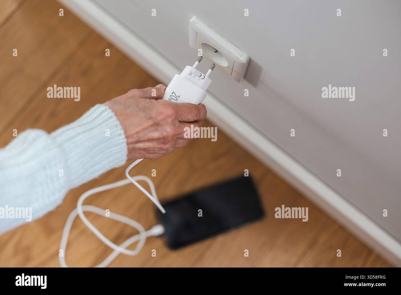 Gros plan d'une femme âgée insérant une fiche d'alimentation dans une prise pour charger son téléphone Banque D'Images