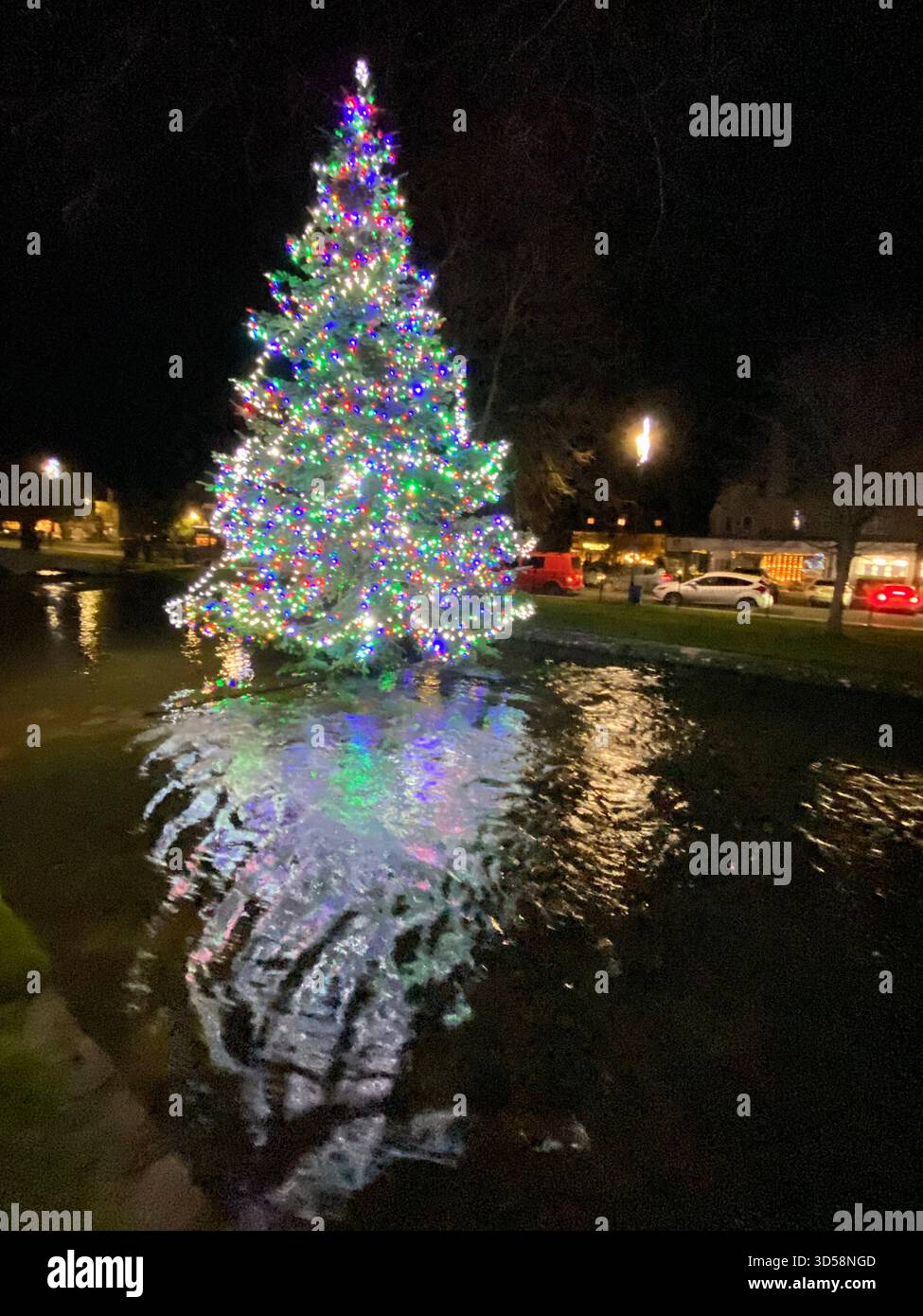 Un arbre de Noël de village se dresse au milieu de la rivière peu profonde Windrush à bouton-on-the-Water, surnommé ;Venise des Cotswolds’ à cause de son - Image de stock capturée avec un smartphone