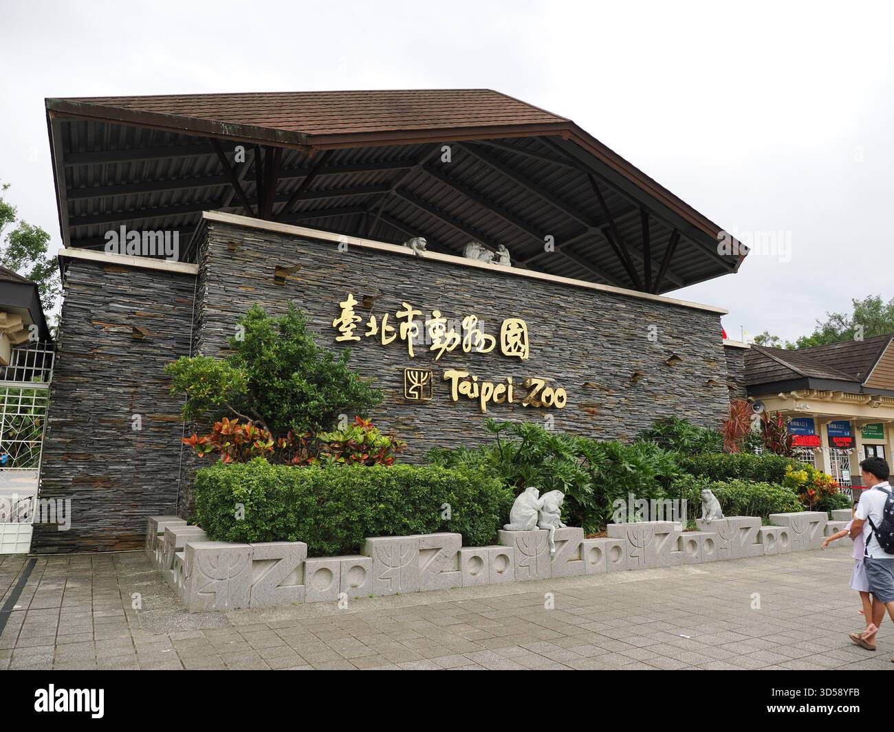 Taipei, Taiwan - 15 novembre 2024 : entrée principale du zoo de Taipei, avec le logo doré sur un mur de pierre et des statues de singe. Banque D'Images