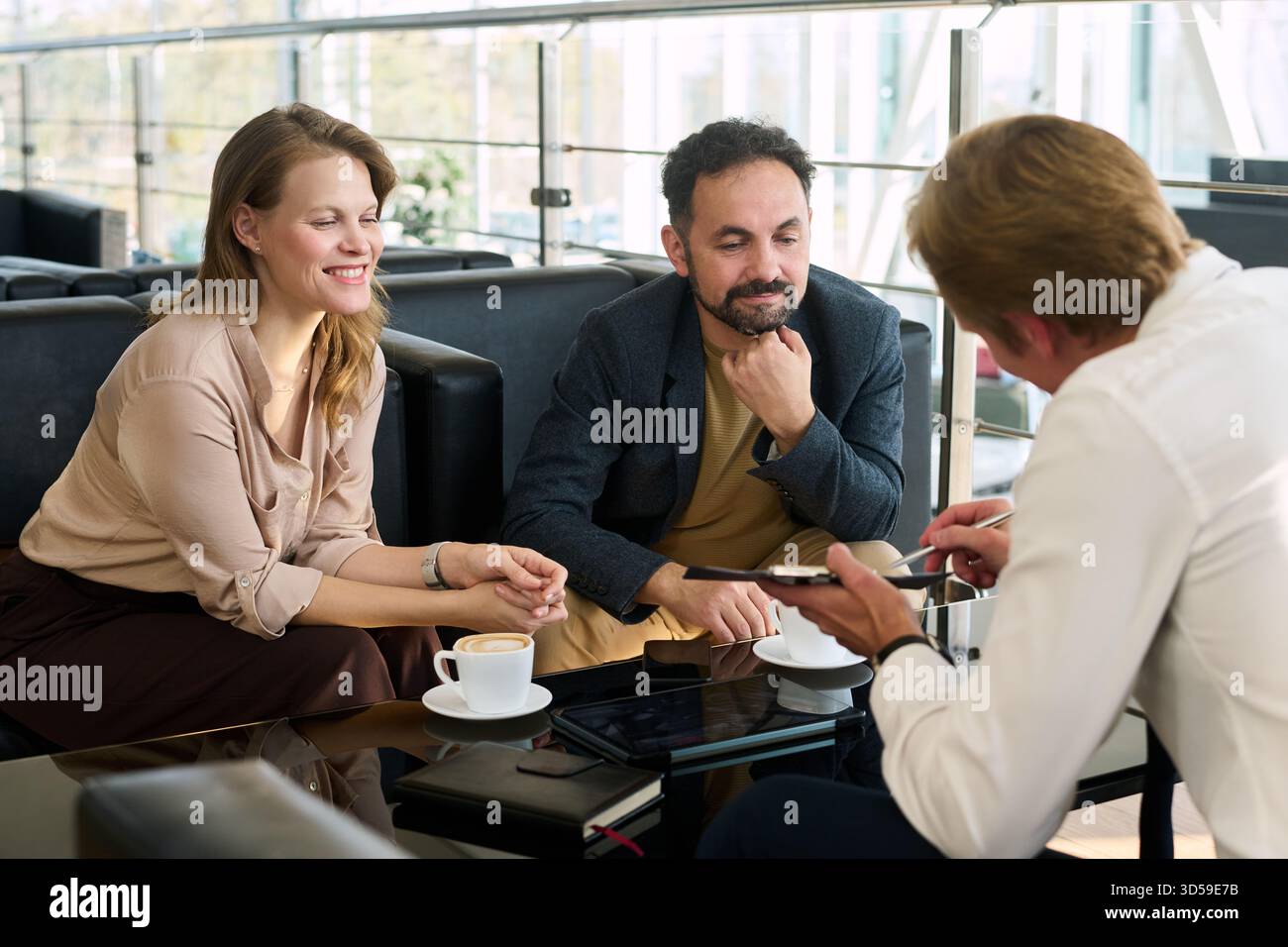 Jeune femme caucasienne et jeune homme du moyen-Orient assis à table écoutant un homme d'âge moyen caucasien expliquant des informations Banque D'Images