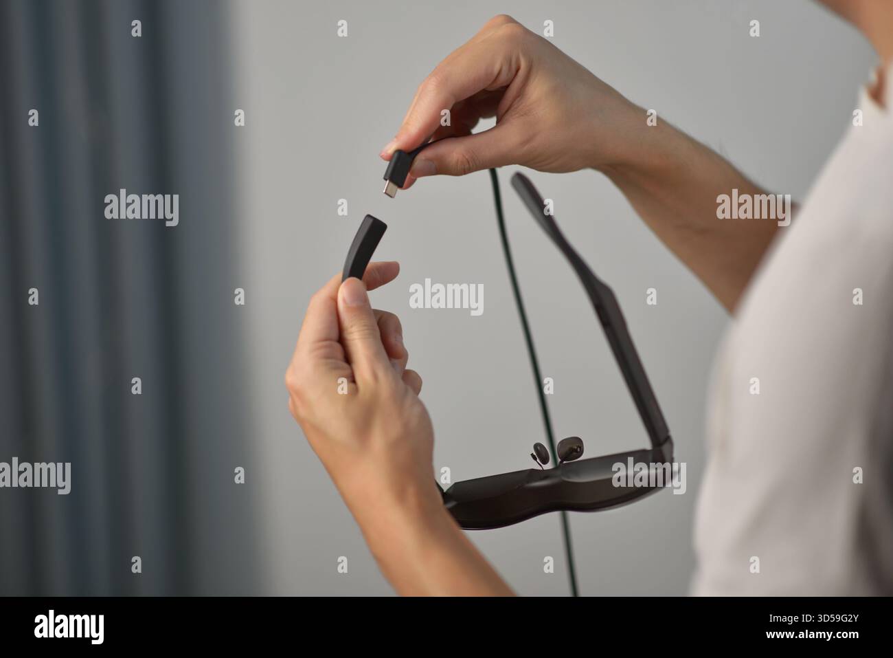 Gros plan des mains branchant un câble USB-C dans des lunettes Smart AR. Concept de technologie moderne, d'appareils portables, de charge, de connectivité et de mode de vie numérique Banque D'Images