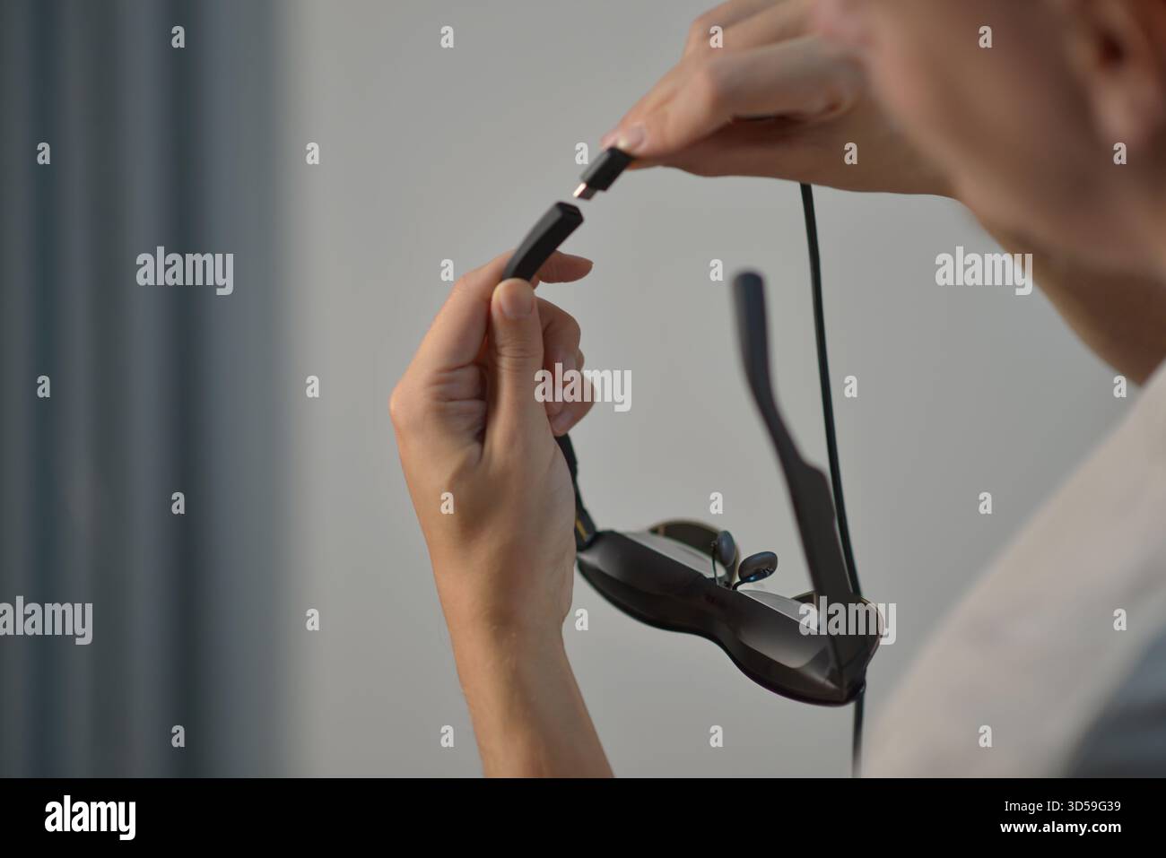 Gros plan des mains branchant un câble USB-C dans des lunettes Smart AR. Concept de technologie moderne, d'appareils portables, de charge, de connectivité et de mode de vie numérique Banque D'Images