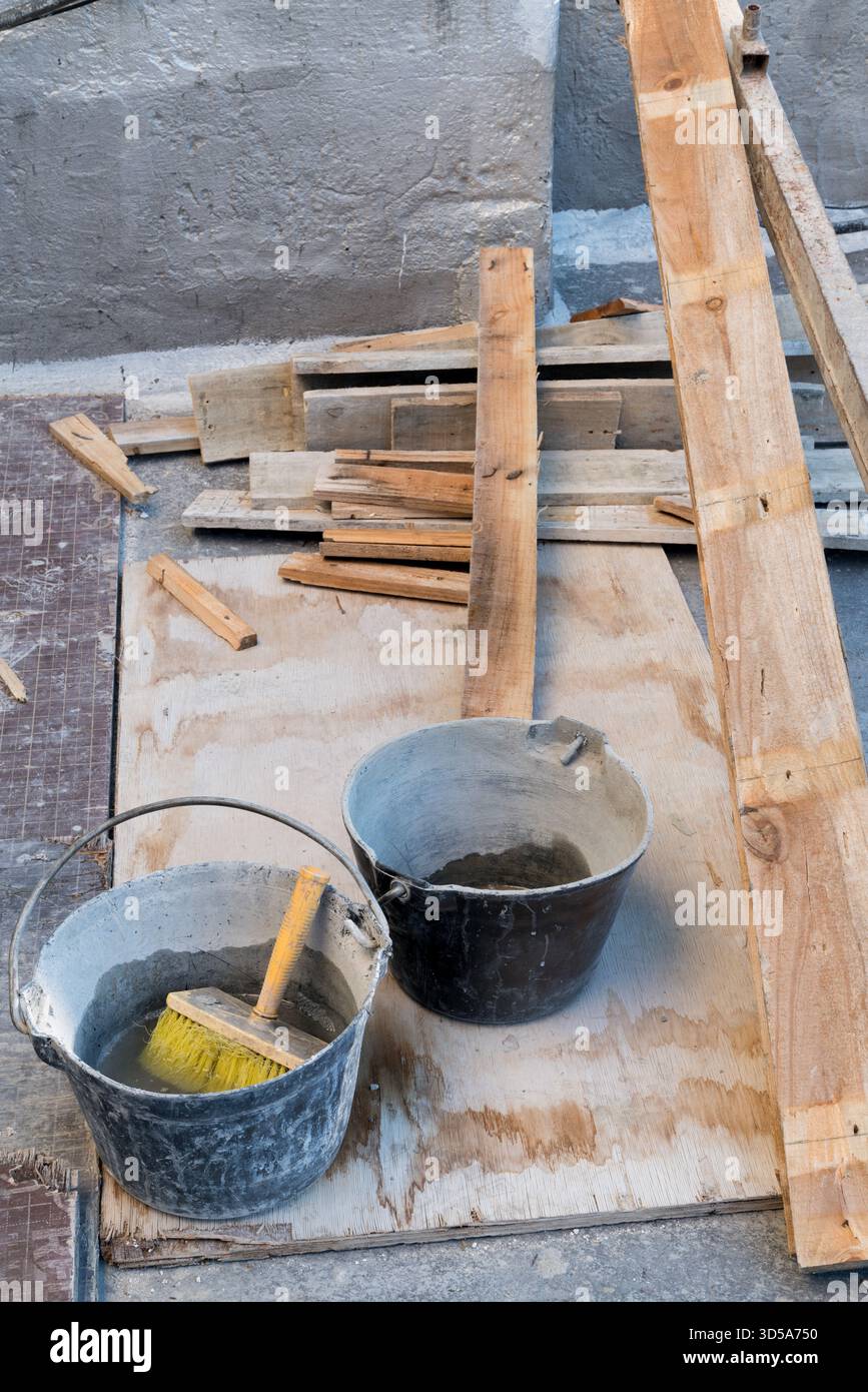 Deux seaux sales et une brosse jaune reposent sur des planches de bois sur le toit d'un chantier Banque D'Images