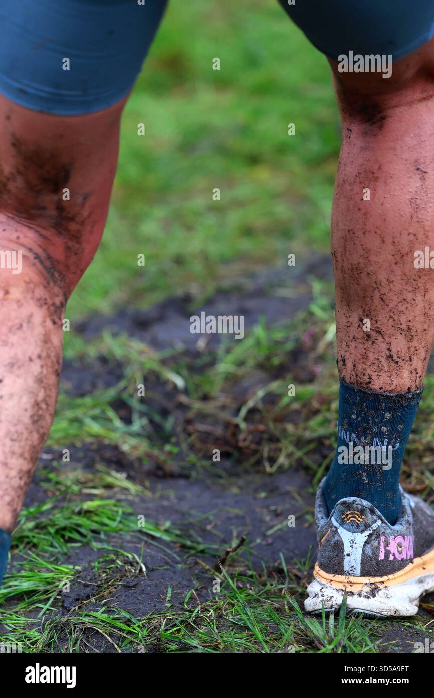 Jambes recouvertes de boue et chaussures de course à pied après une course en plein air difficile Banque D'Images