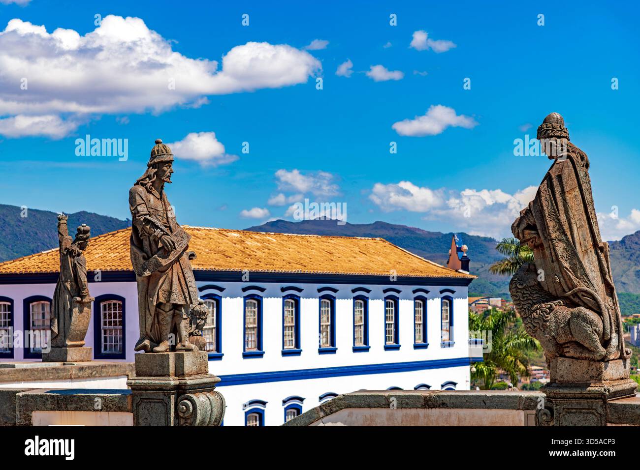 Statues de prophètes bibliques sculptées par Aleijadinho avec des bâtiments anciens et des montagnes en arrière-plan à Congonhas, Minas Gerais. Banque D'Images