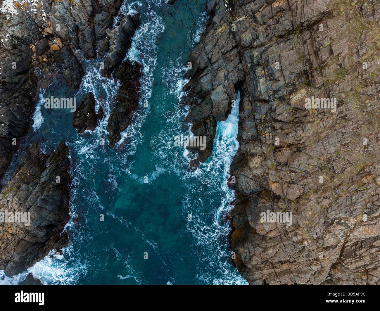 De puissantes vagues se précipitent contre des falaises abruptes tandis que l'eau turquoise scintille sous le soleil, mettant en valeur la beauté de la nature sur le littoral à l'arrière Banque D'Images