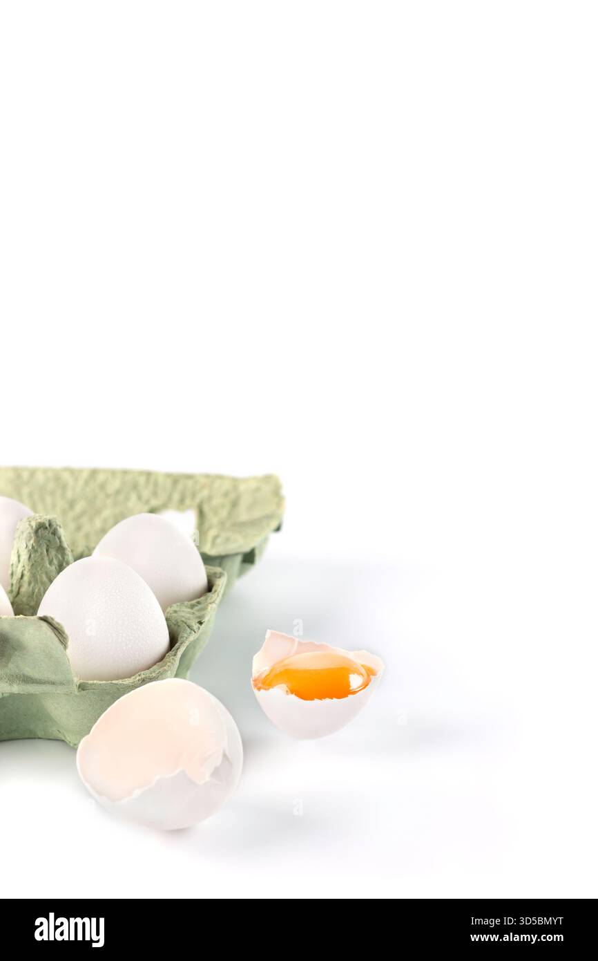 Un carton contient plusieurs oeufs frais, avec un oeuf cassé ouvert à côté, montrant un jaune vif. La scène est placée sur un fond blanc propre, Banque D'Images
