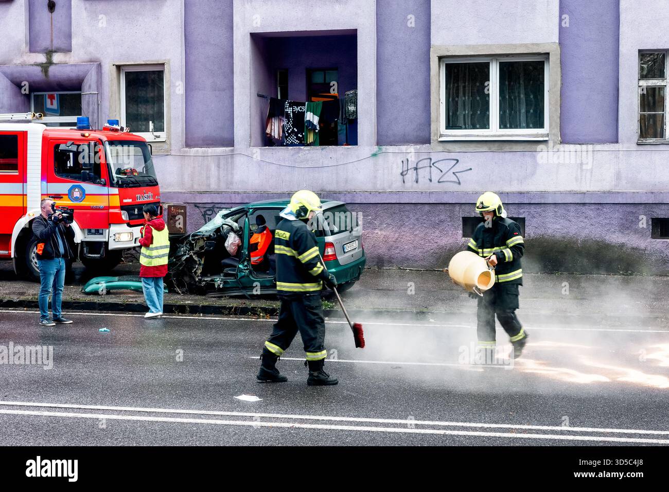 Ruzomberok, Slovaquie - 11 octobre 2025 : les pompiers nettoyent la route après un grave accident de voiture avec l'équipe d'urgence et un véhicule endommagé pendant le sauvetage opérée Banque D'Images